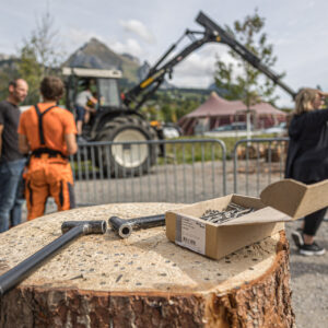 Ein Nagelstock mit Hammer und Nägeln, im Hintergrund ein Forstwart mit dem Forsttraktor