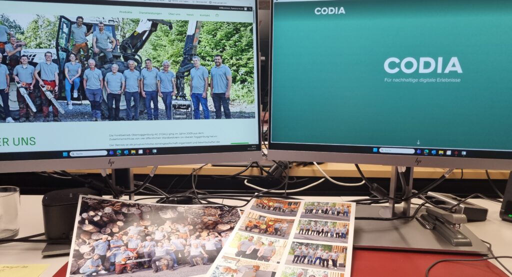 Zwei Computerbildschirme zeigen die neue Homepage der FOAG und die Homepage der Codia GmbH. Davor liegen Fotos von Fotoclick Arlette Geisser.